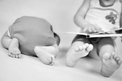 Little girl is reading a book tog her baby brother. Black and white photo with soft focus on their feet. Family values