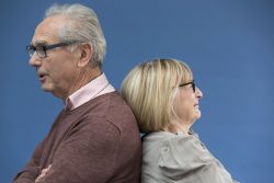 Portrait of mature couple standing back to back looking away on blue background. Istockalypse Paris 2016